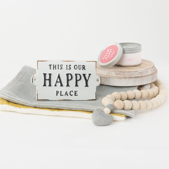 Collection of gift box items includes a candle, happy place sign and wooden beads