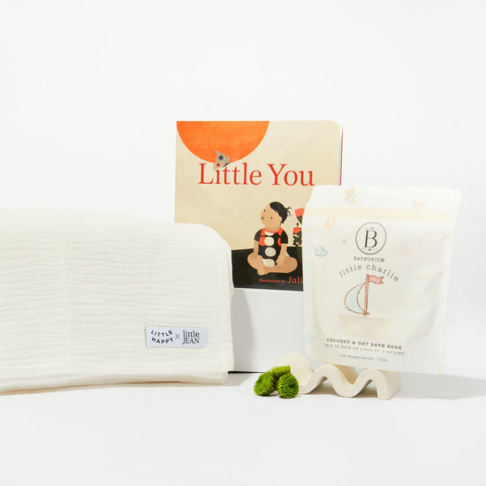 Collection of gift box items includes a a book, white swaddle and bath soak